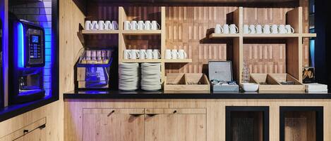 Una estación de café con una máquina de café, pilas de platos y varias tazas de café sobre estantes de madera.
