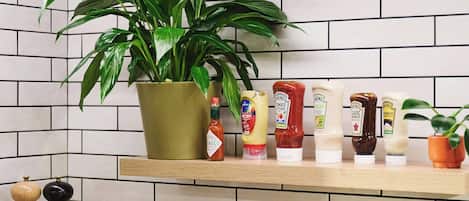 Una cocina con estufa negra, ollas, una planta en maceta y botellas de condimentos en un estante.
