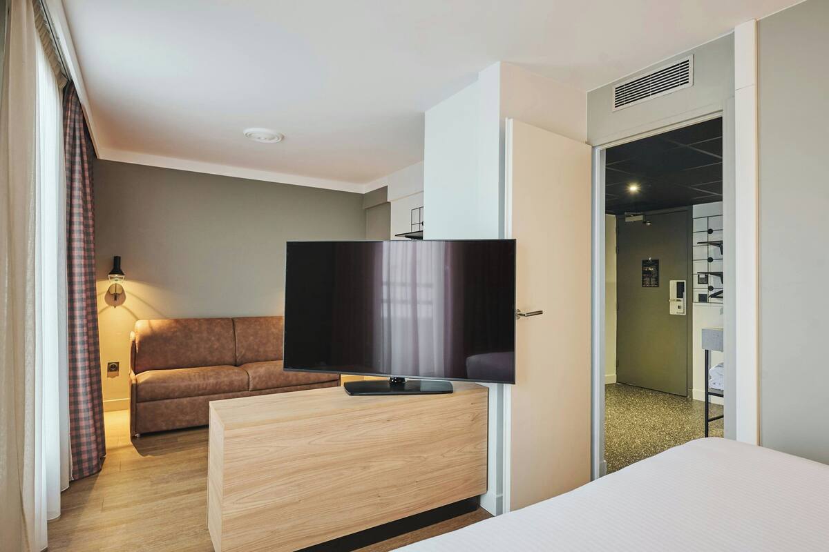 Une chambre d’hôtel moderne avec une commode en bois, un téléviseur à écran plat, un canapé et un lit.