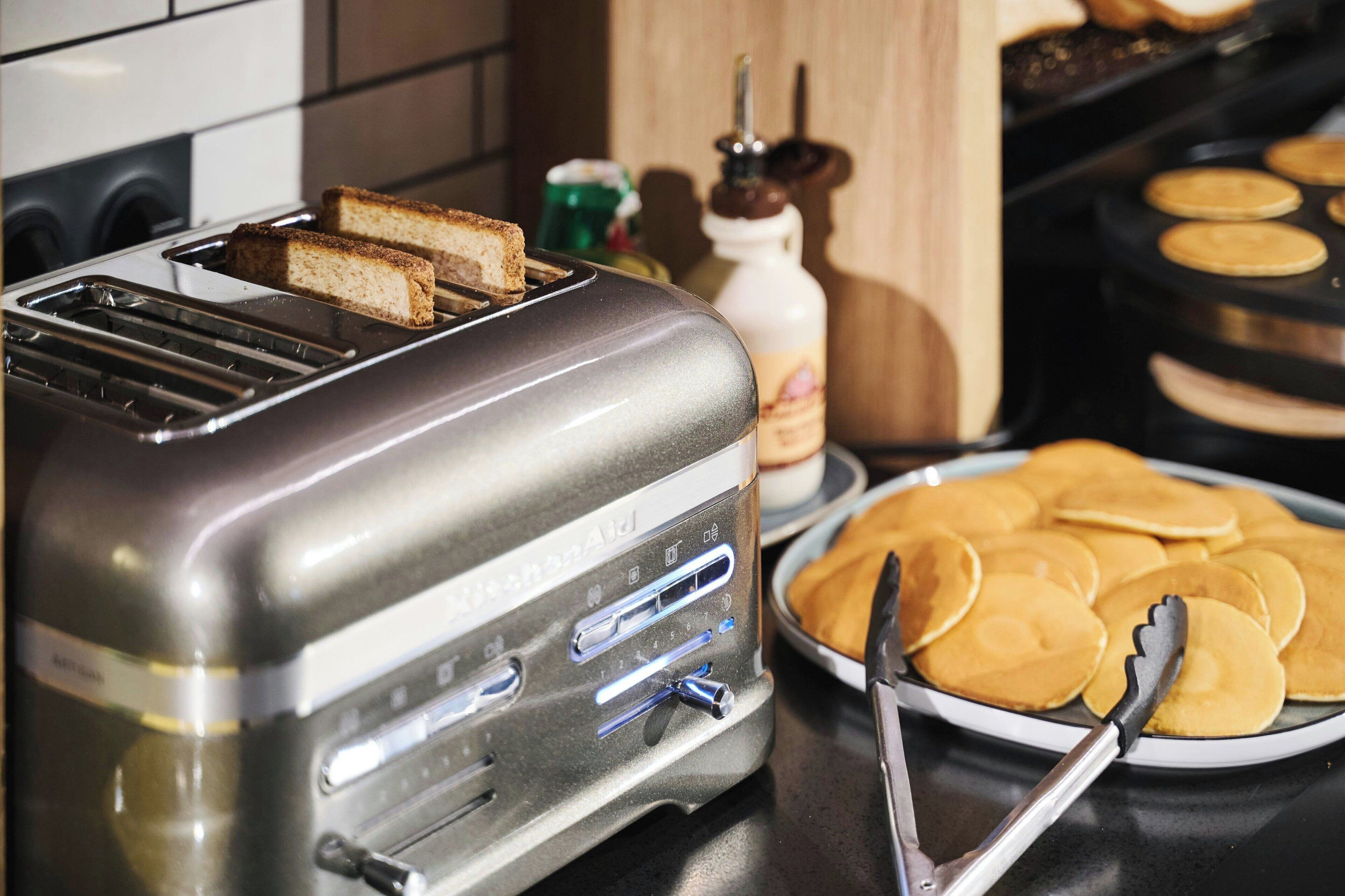 A kitchen with a toaster, a plate of pancakes, and a bottle of syrup.