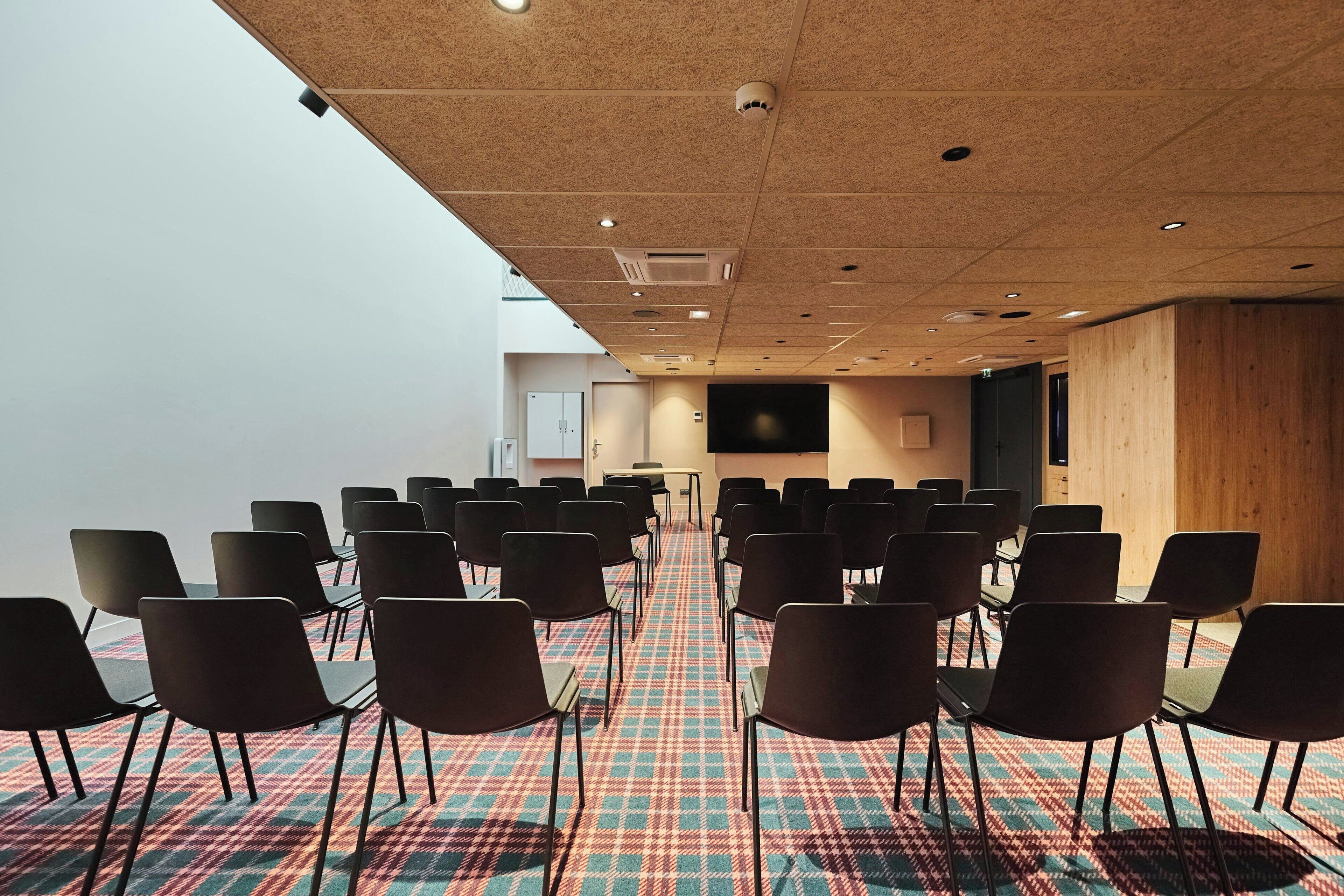 Une salle de conférence avec des rangées de chaises, une moquette à motifs et un mur en bois.