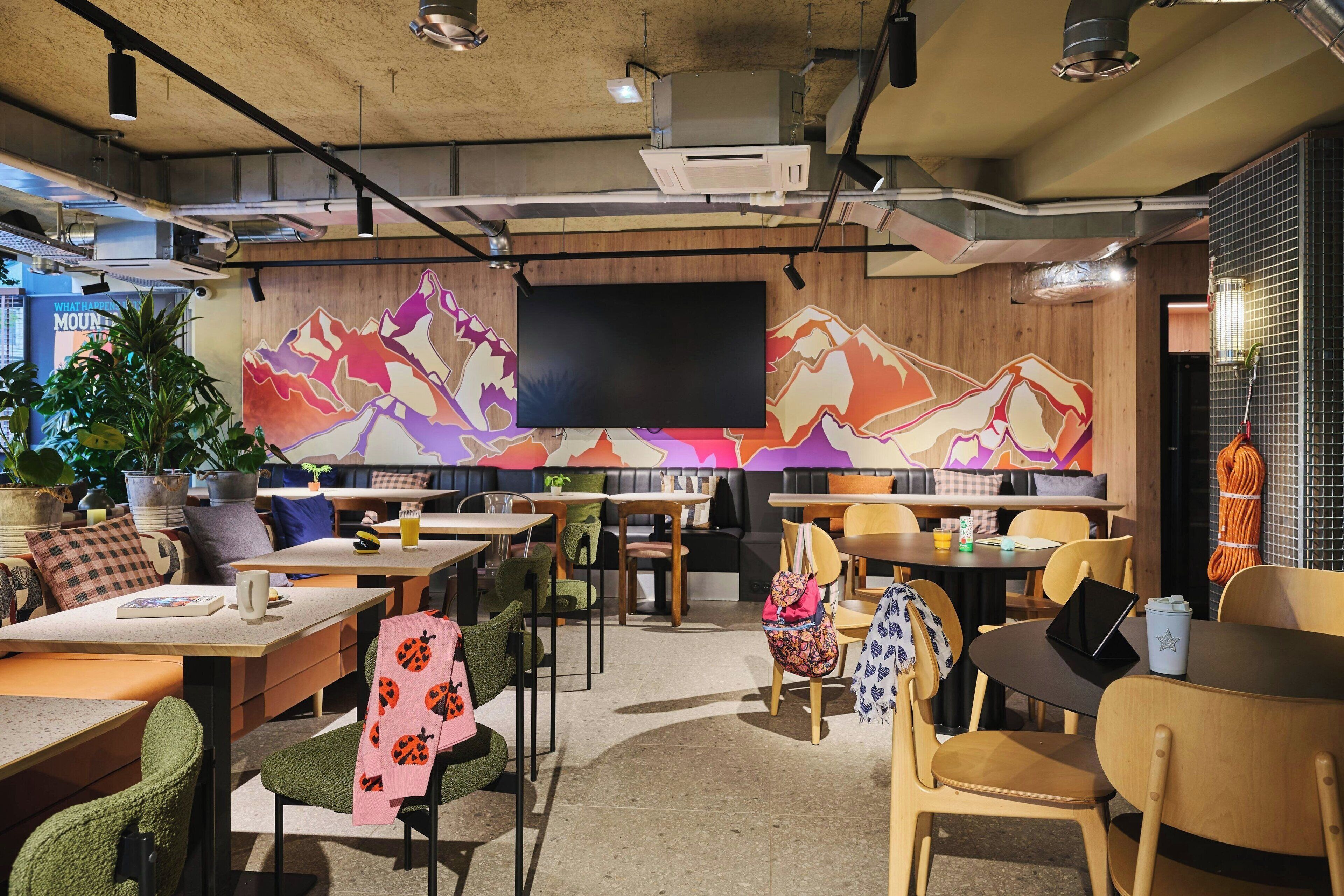 A modern cafe with wooden tables, chairs, and a large mural on the wall.