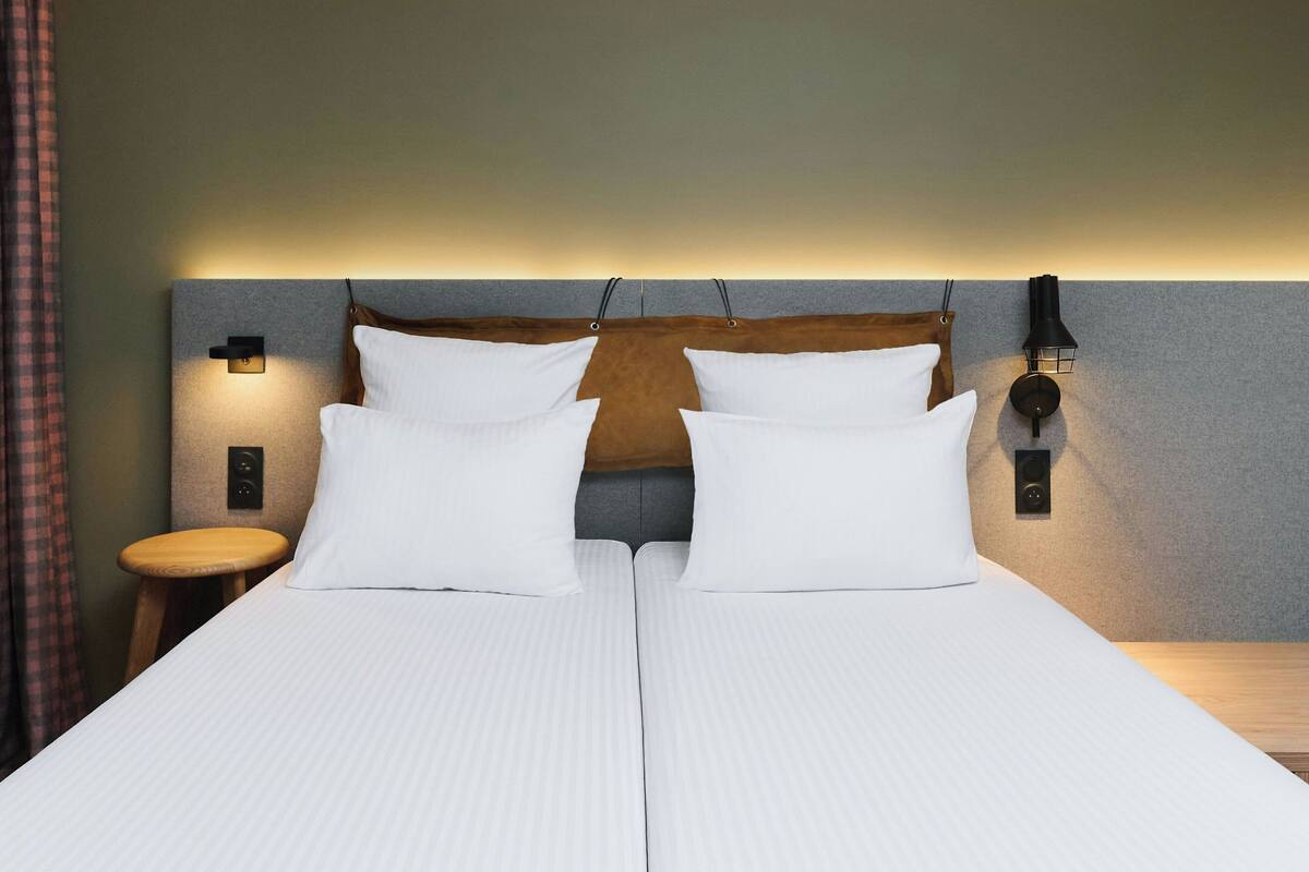 Un lit double avec du linge de lit blanc, une tête de lit en bois et deux lampes de chevet.