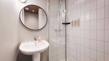 A modern bathroom with a white sink, a round mirror, and a glass-enclosed shower area.