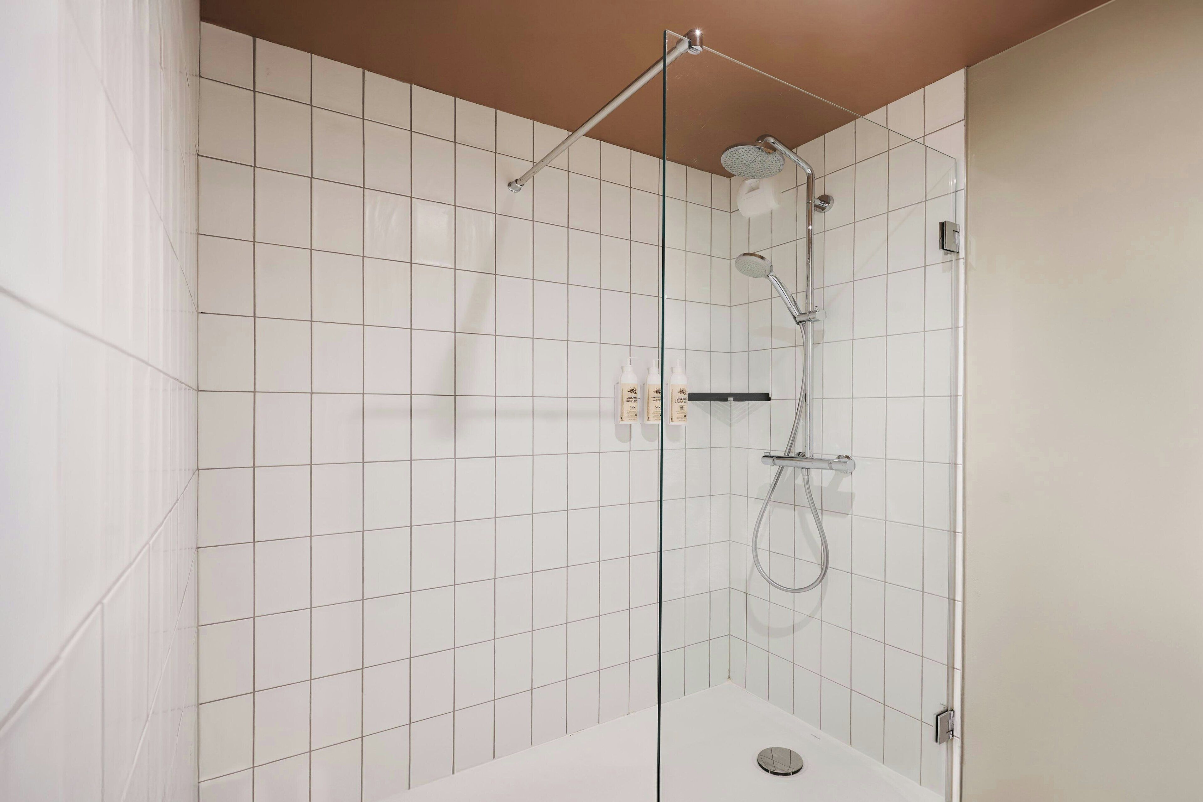 A modern shower area with a glass door, white tiled walls, and a handheld showerhead.
