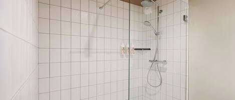 Un área de ducha moderna con mampara de vidrio, paredes de azulejos blancos y un cabezal de ducha de mano.