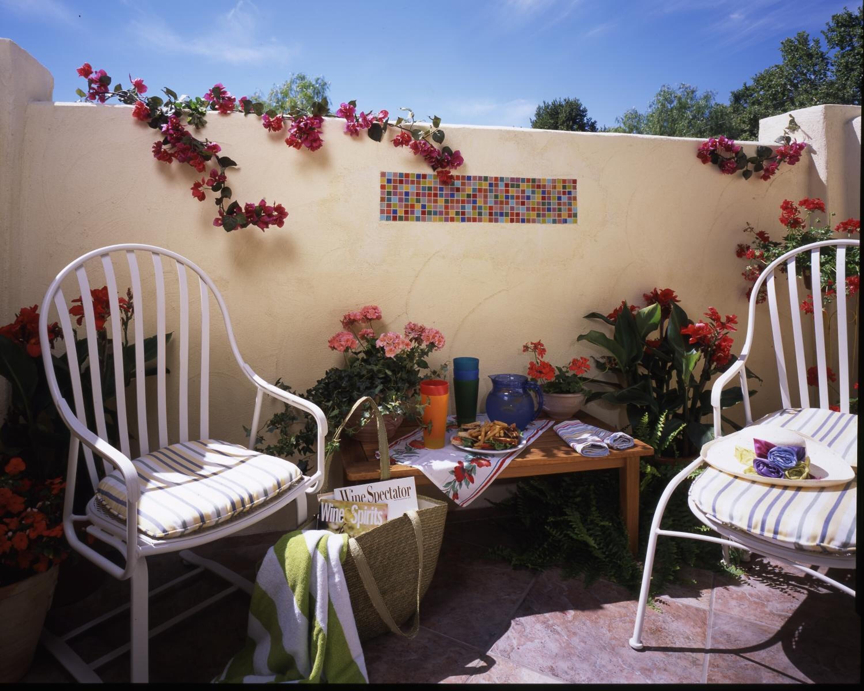 A patio with two white chairs, a small table with a wine glass, and a mosaic wall.