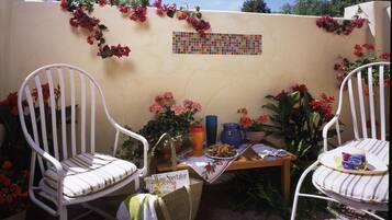 A patio with two white chairs, a small table with a wine glass, and a mosaic wall.