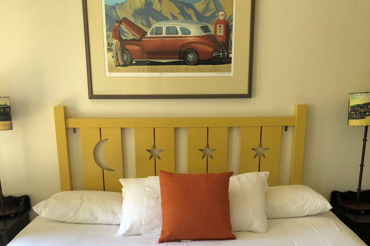 A bed with white bedding, a yellow headboard with star decorations, and a framed painting of a car on the wall.