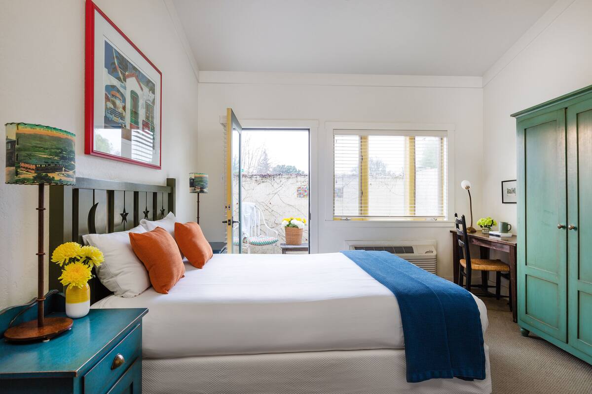 A bedroom with a bed, bedside table, dresser, and a window.
