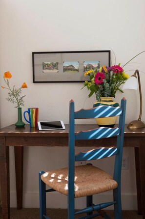 Un escritorio de madera con una tableta, un florero con flores, una taza y una foto en un marco en la pared.