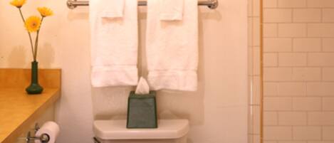 Ein Badezimmer mit Toilette, einem Handtuchhalter mit zwei Handtüchern, einem gerahmten Bild der Golden Gate Bridge, einer Toilettenpapierrolle und einer Schachtel auf dem Toilettendeckel.