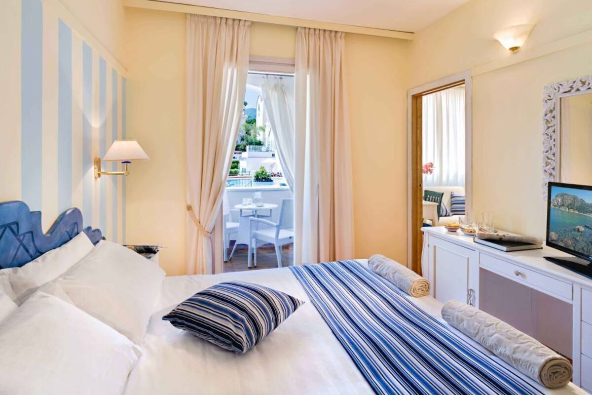 A hotel room with a bed, a desk with a chair, a TV, and a balcony with a view of the outside.