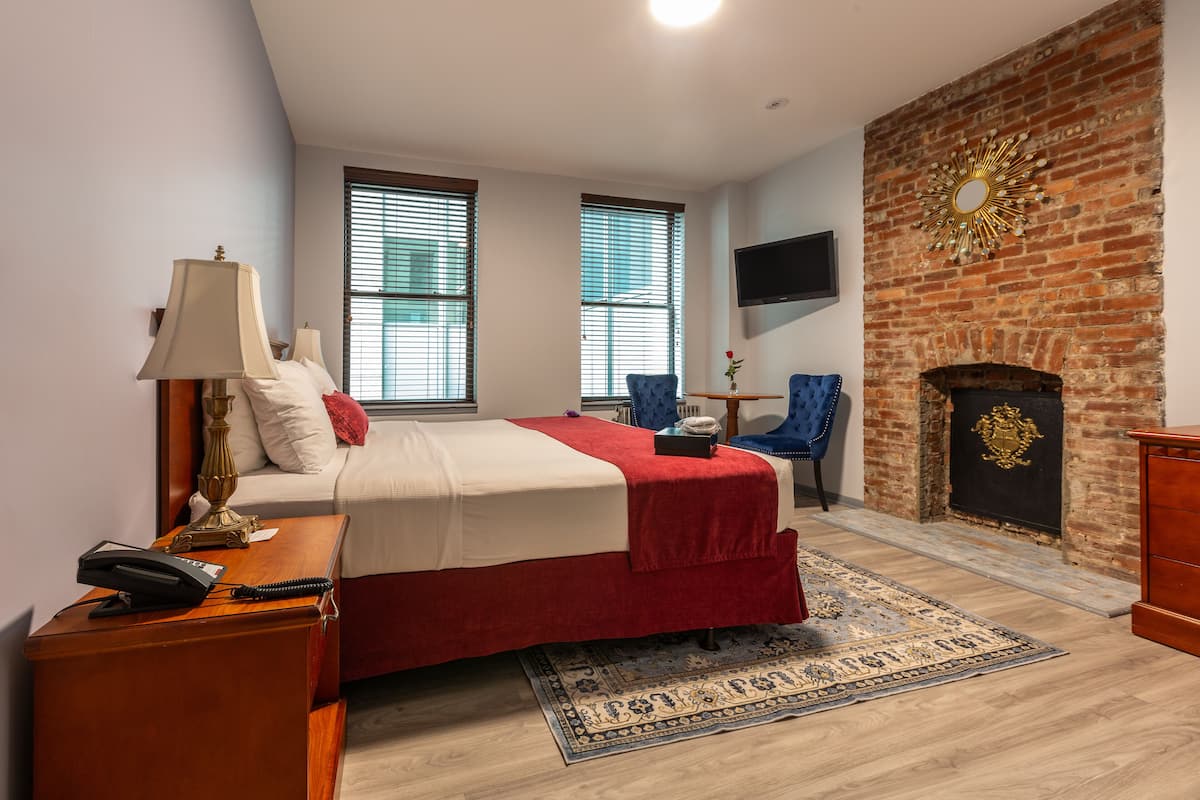 A bedroom with a bed, a desk, a chair, a fireplace, and a TV mounted on the wall.