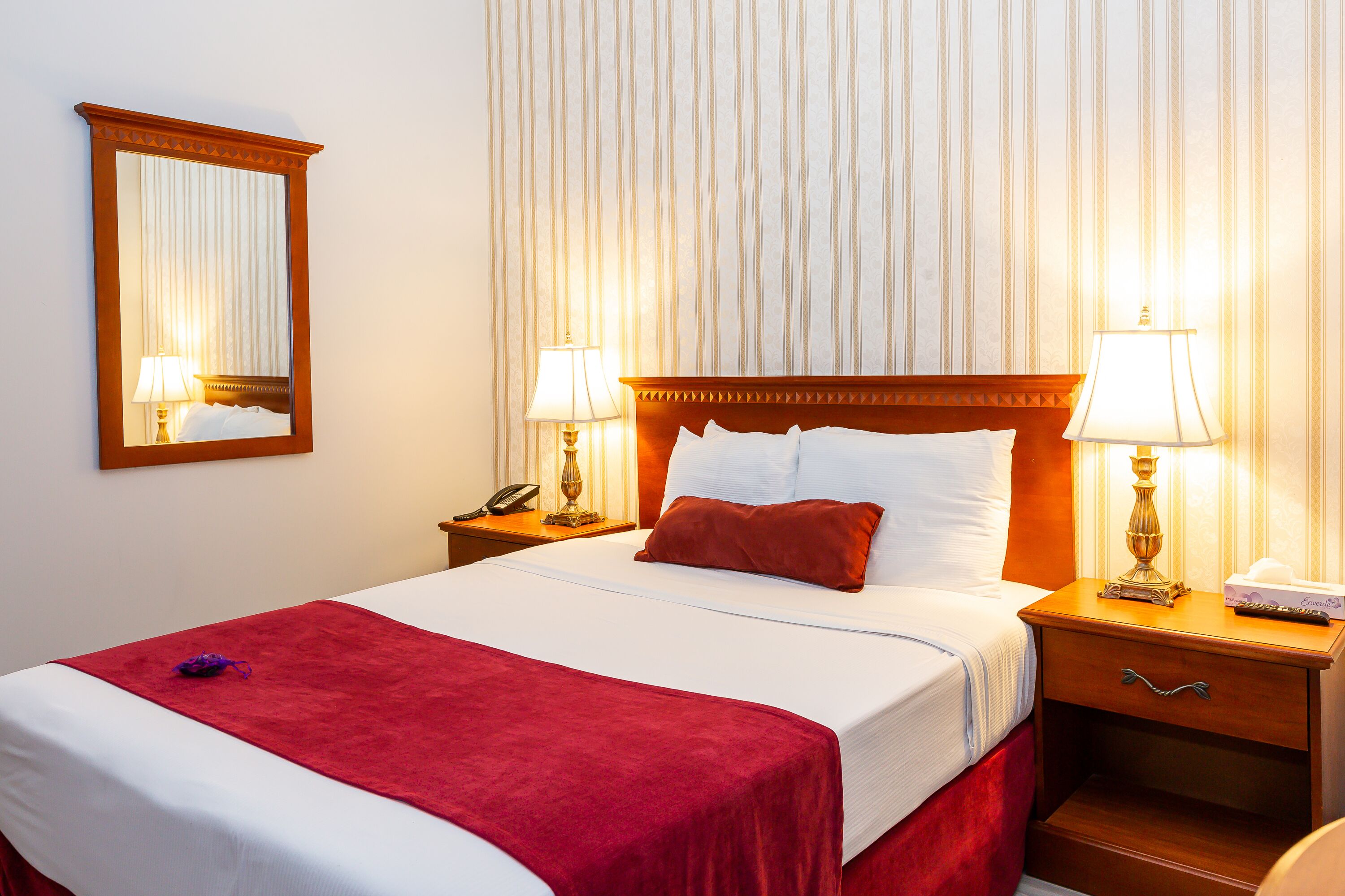 Ein Hotelzimmer mit einem großen Bett, zwei Nachttischen, einem Schminktisch, einem Spiegel und rahmiger Tapete.