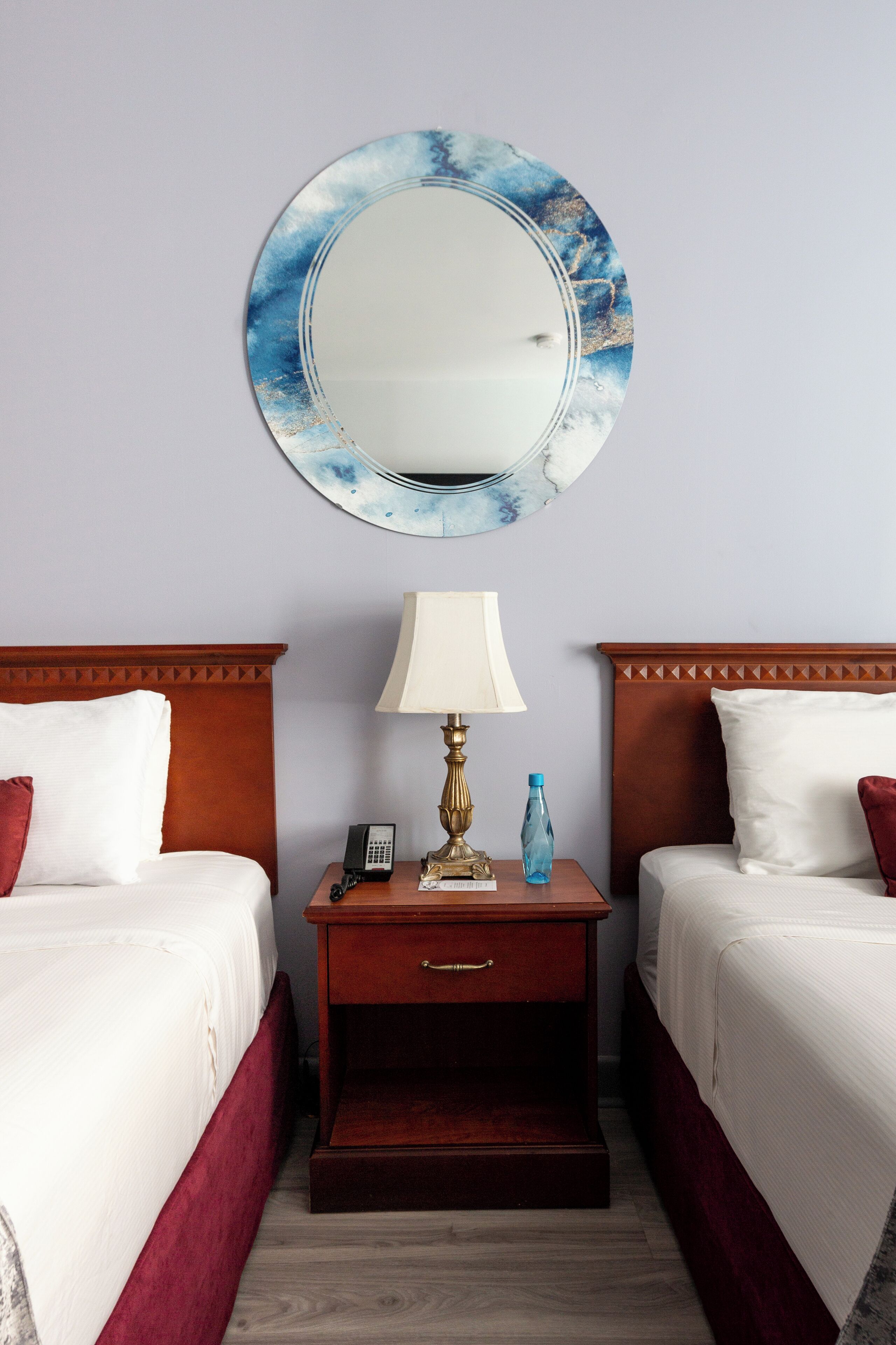 Ein Hotelzimmer mit zwei Betten, einem Nachttisch mit Lampe, einem Spiegel und einem kleinen Tisch mit Telefon und Flasche.