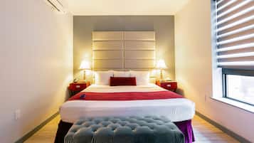 Une chambre d’hôtel avec un grand lit, deux tables de chevet avec des lampes, une fenêtre avec des stores et un plancher en bois.