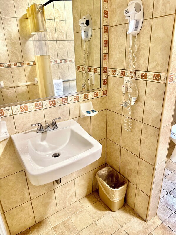 A bathroom with a sink, a mirror, a hairdryer, and a trash bin.