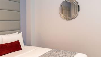 A neatly made bed with a patterned bedspread, a red pillow, and a folded white towel on a wooden nightstand.
