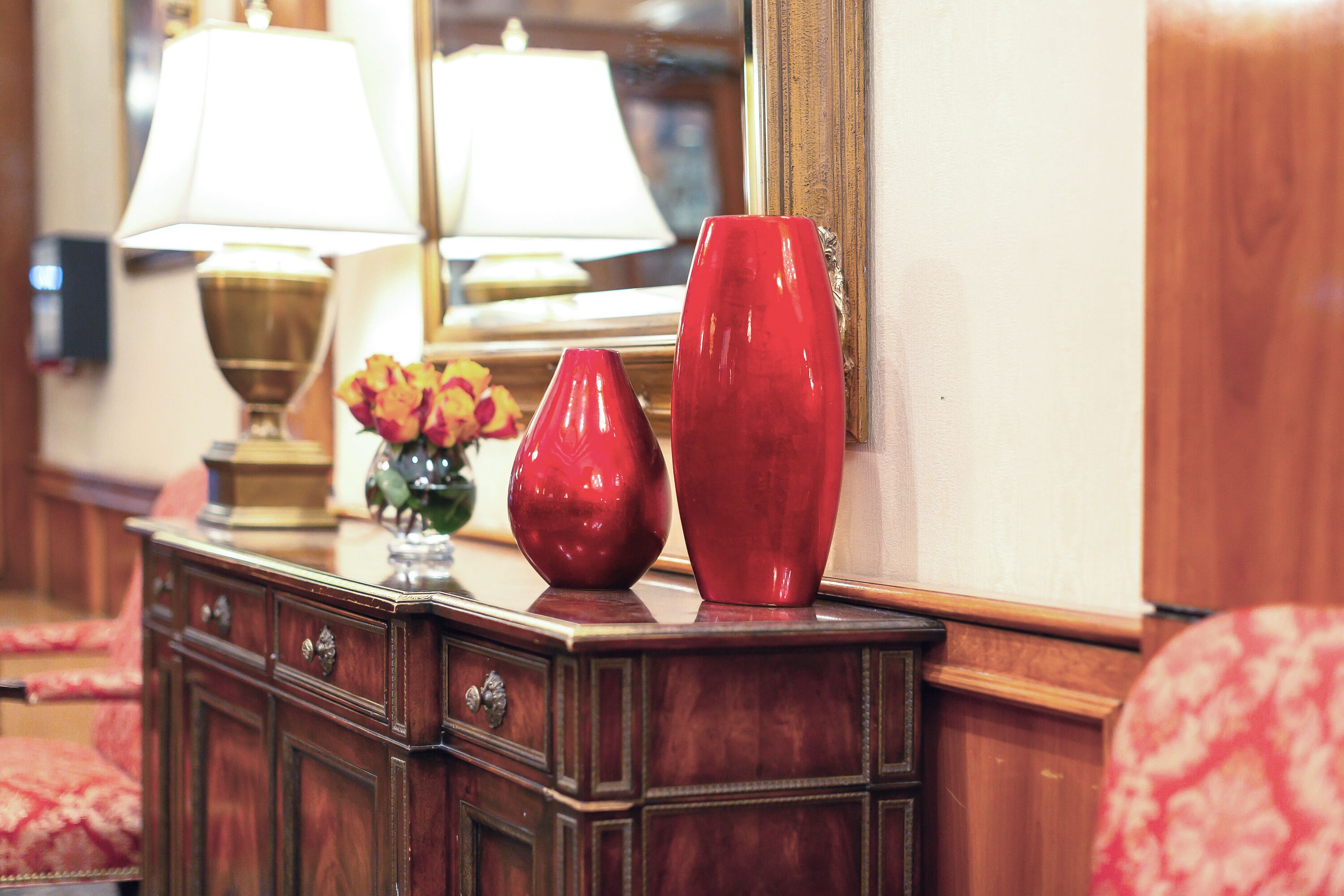 A wooden dresser with two red vases and a lamp.