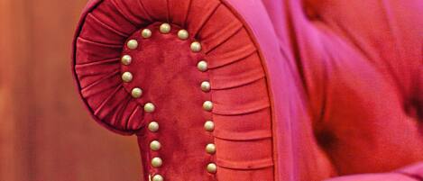 Primer plano de una butaca tapizada en rojo con respaldo capitonado y botones decorativos.