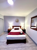 Een verzorgde hotelkamer met een groot bed, twee nachtkastjes met lampen, een spiegel aan de muur en een decoratieve plafondlamp.