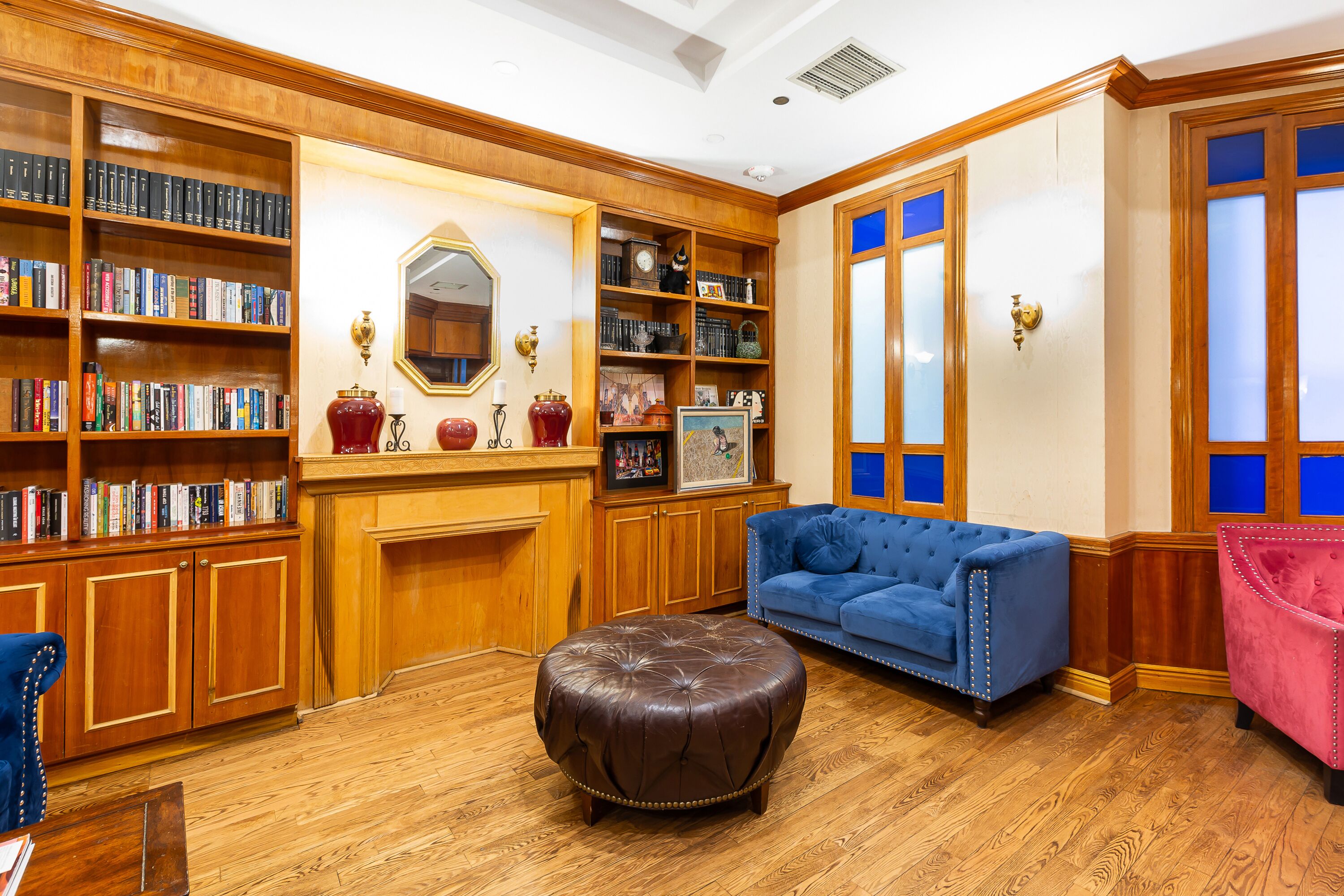 Una biblioteca con estanterías de madera, un sofá azul, un reposapiés marrón y una silla roja.