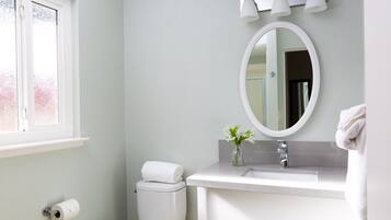 A bathroom with a toilet, sink, mirror, and a window.