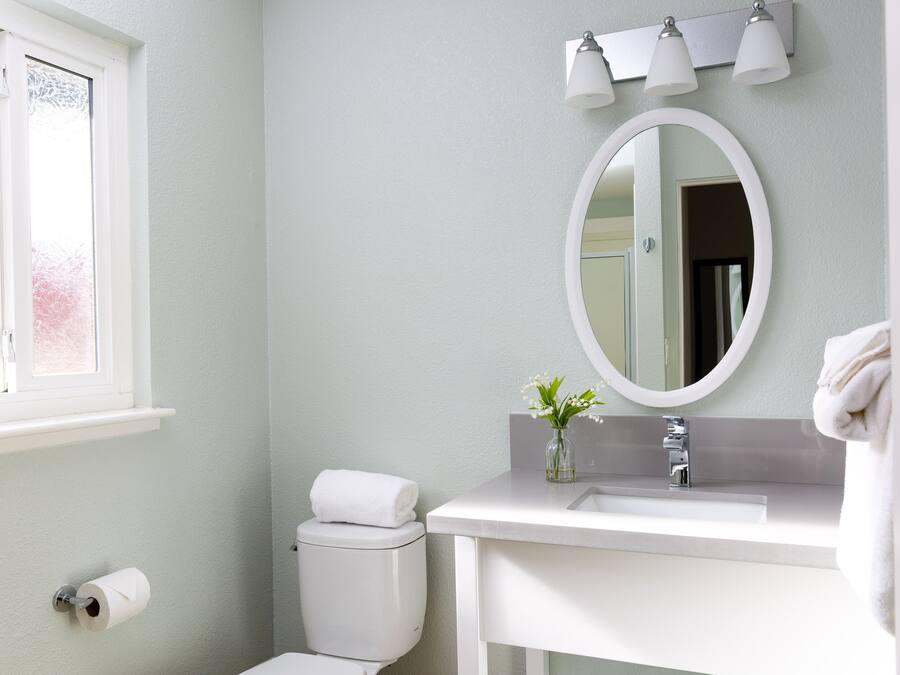 A bathroom with a toilet, sink, mirror, and a window.