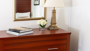Une commode en bois avec trois tiroirs, un miroir, une lampe et un panier contenant des serviettes.
