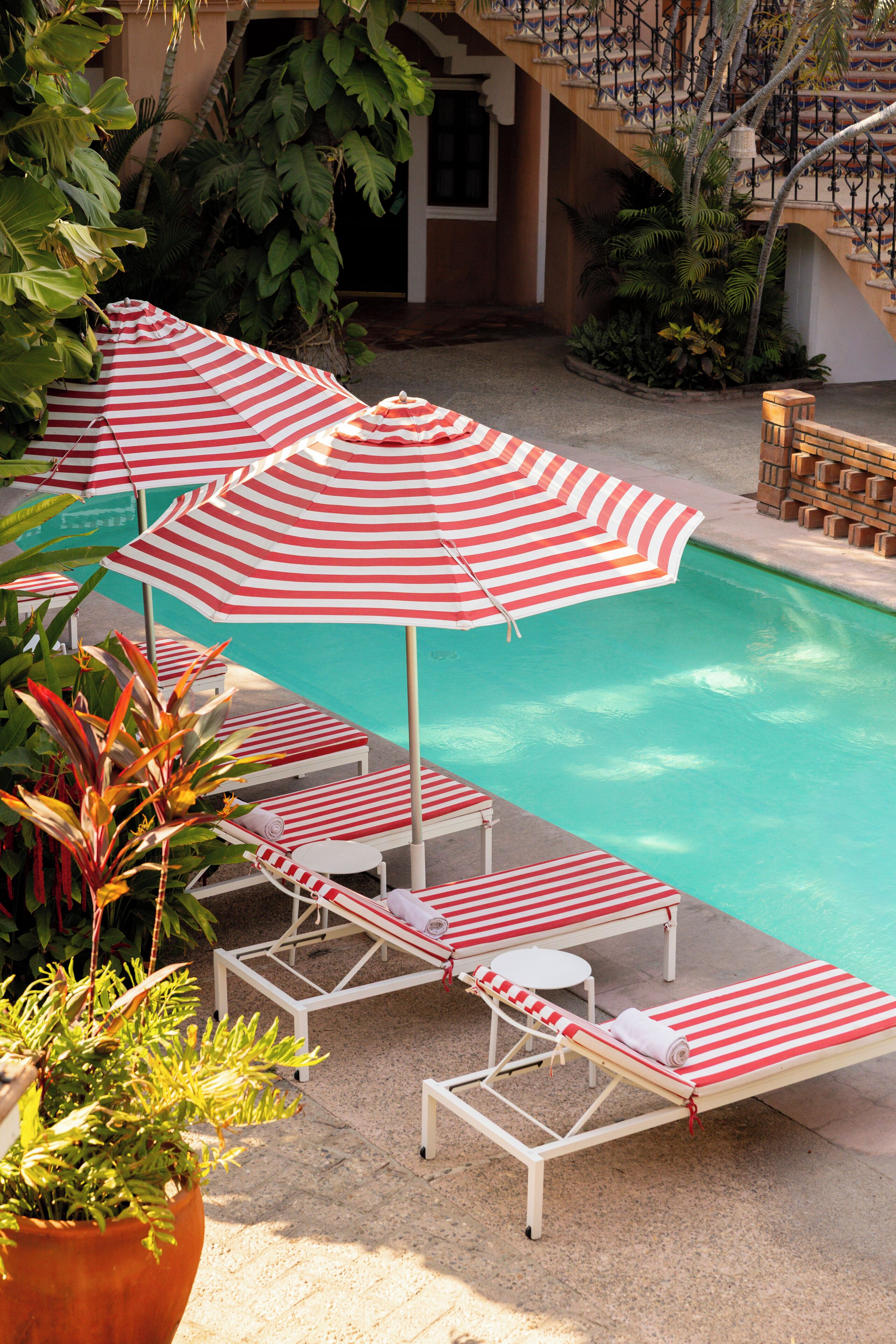A pool area with striped umbrellas, lounge chairs, and potted plants.