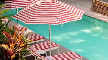 A pool area with striped umbrellas, lounge chairs, and potted plants.
