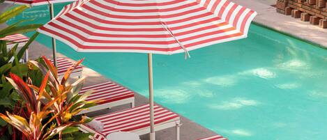 A pool area with striped umbrellas, lounge chairs, and potted plants.