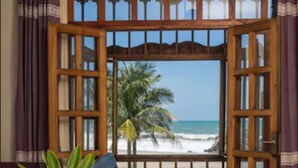 Una habitación con un ventanal grande que da a una playa, una mesa de madera con un florero y un sofá.