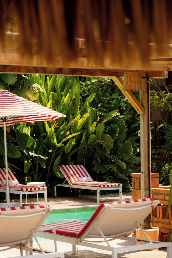 A poolside area with lounge chairs and a striped umbrella. - Hotel Santa Fe (Puerto Escondido)