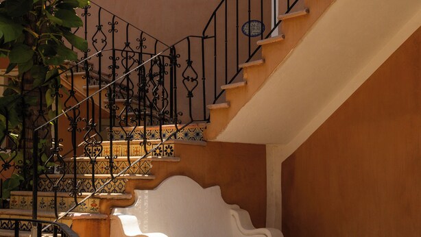 A staircase with a wrought iron railing, a white bench, and a potted plant.