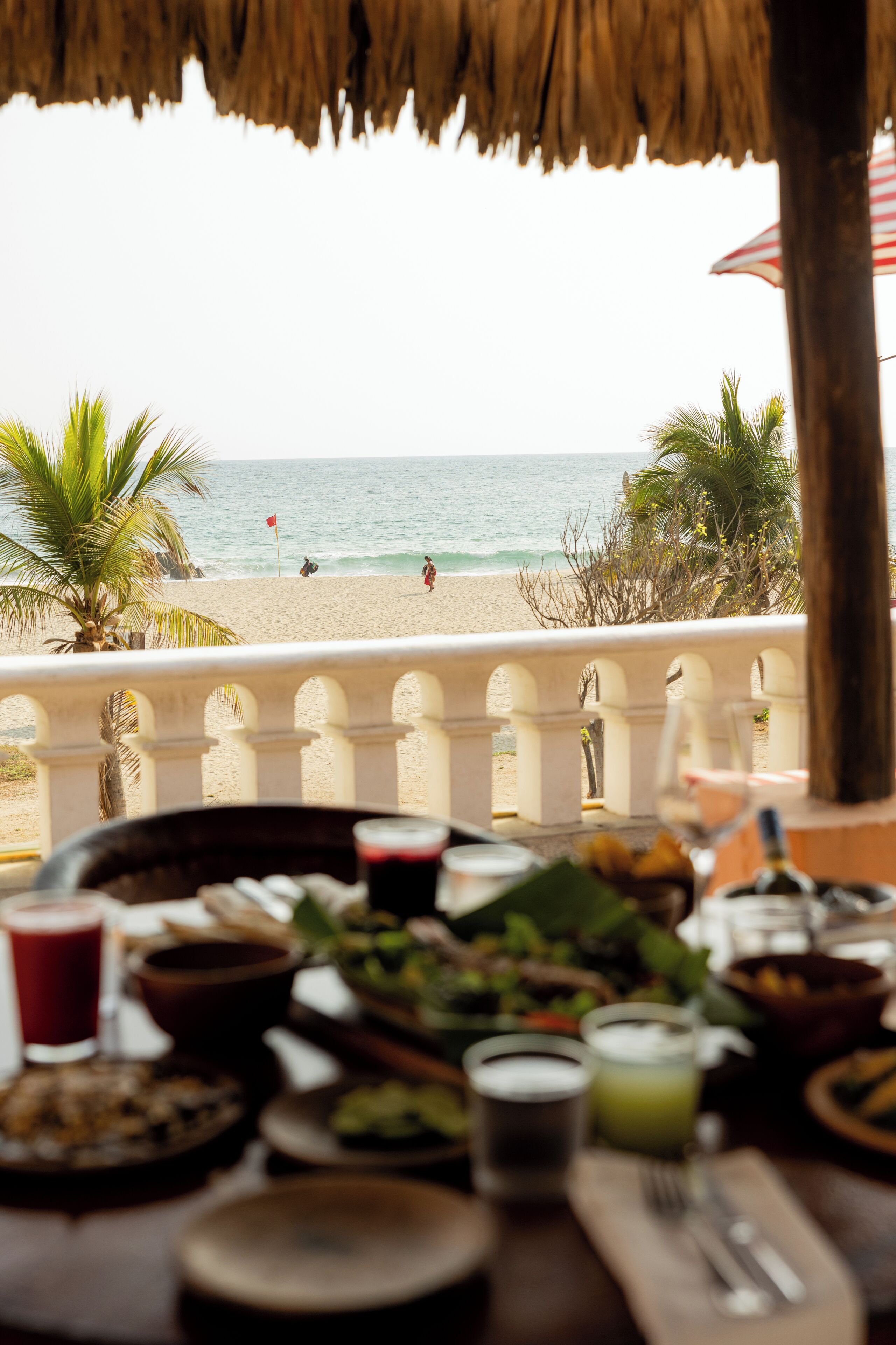 Une table dressée avec de la nourriture et des boissons, donnant sur une plage bordée de palmiers et sur l’océan.