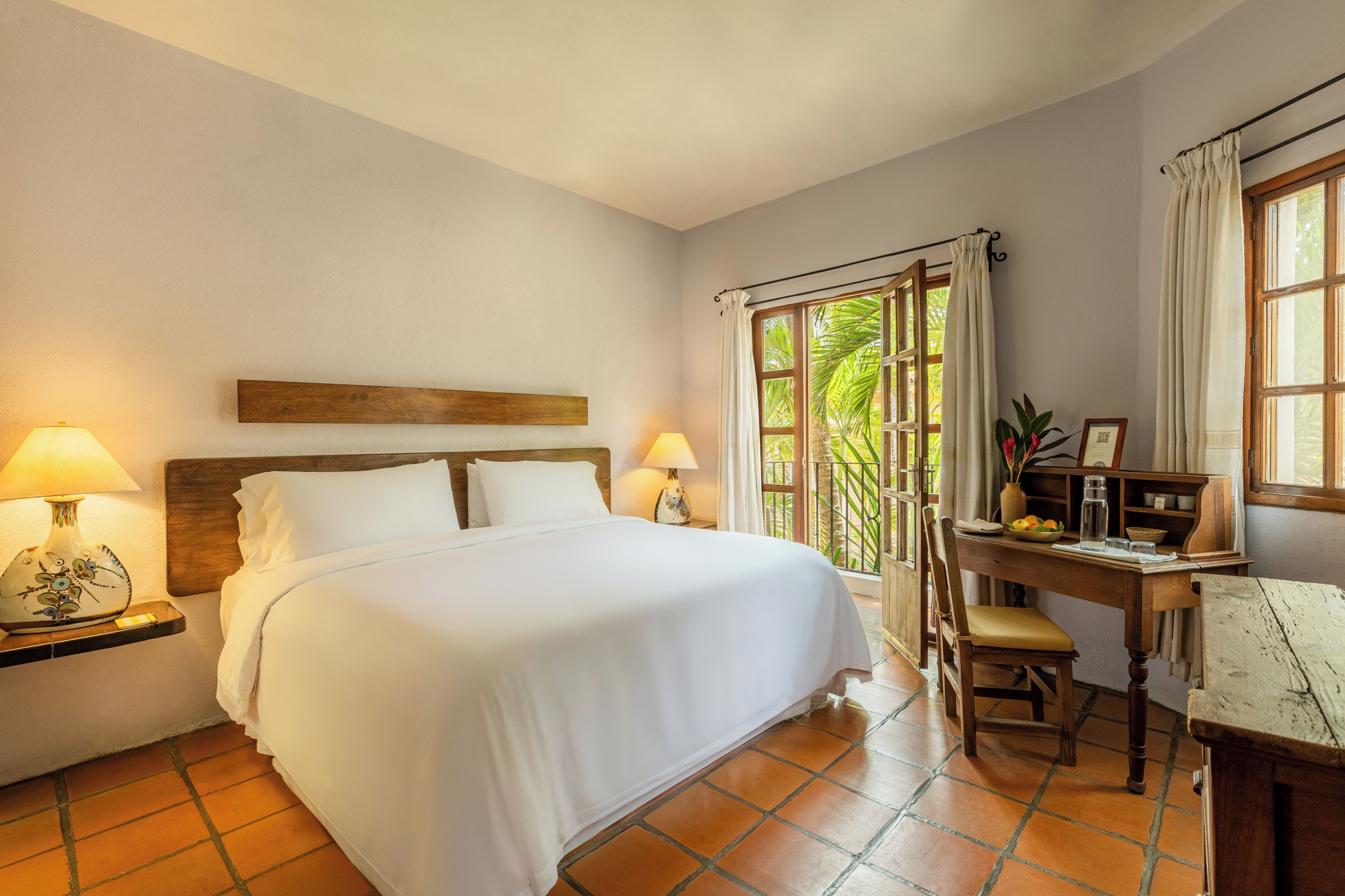 Habitación de hotel con cama, lámparas de noche, un escritorio con silla y ventana con cortinas.