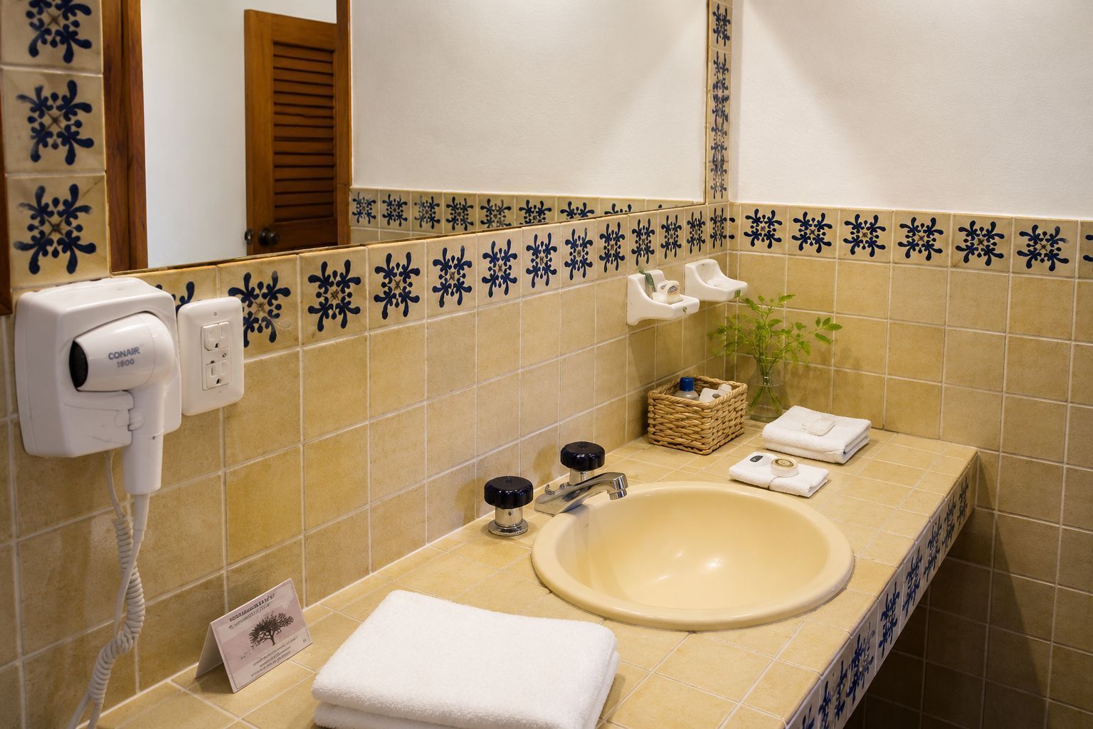 A bathroom with a beige sink, a hairdryer, a mirror, and a towel rack.