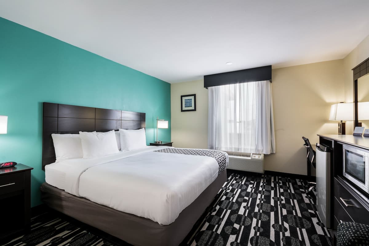 A hotel room with a large bed, a desk, a chair, a TV, and a window with curtains.