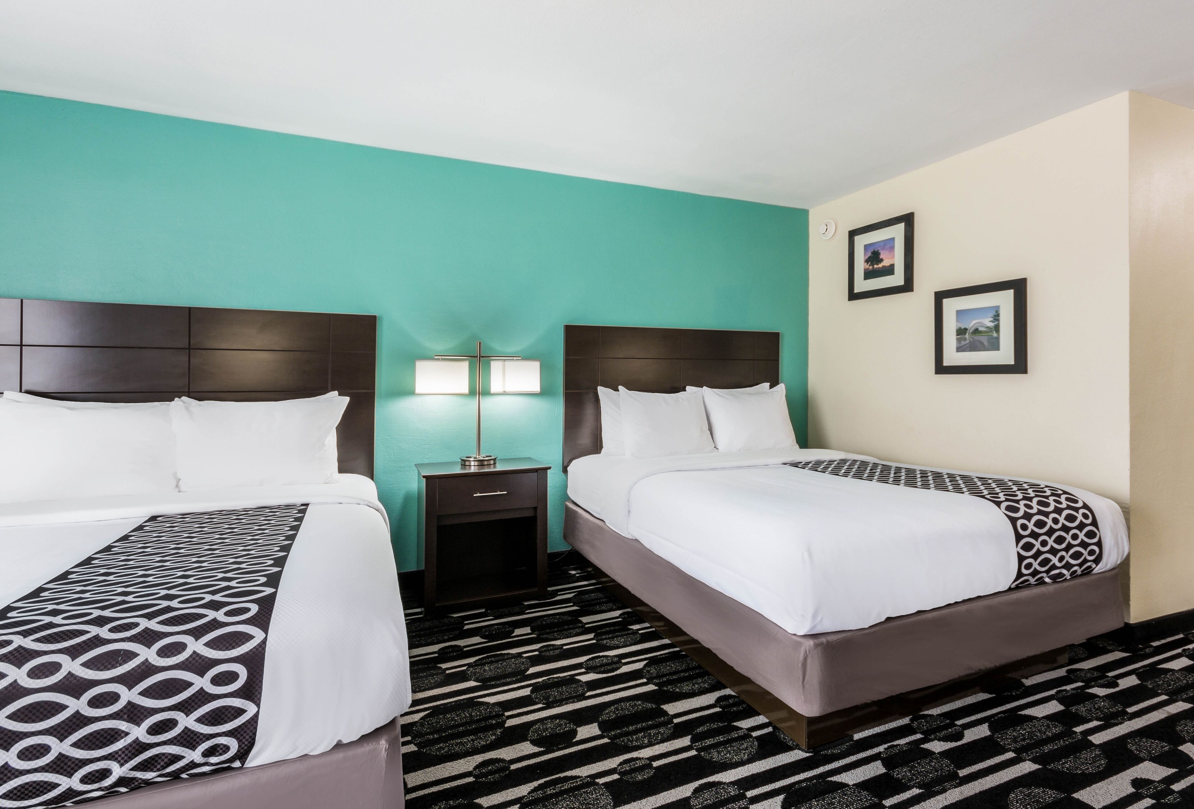 A hotel room with two beds, a nightstand with a lamp, and two framed pictures on the wall.