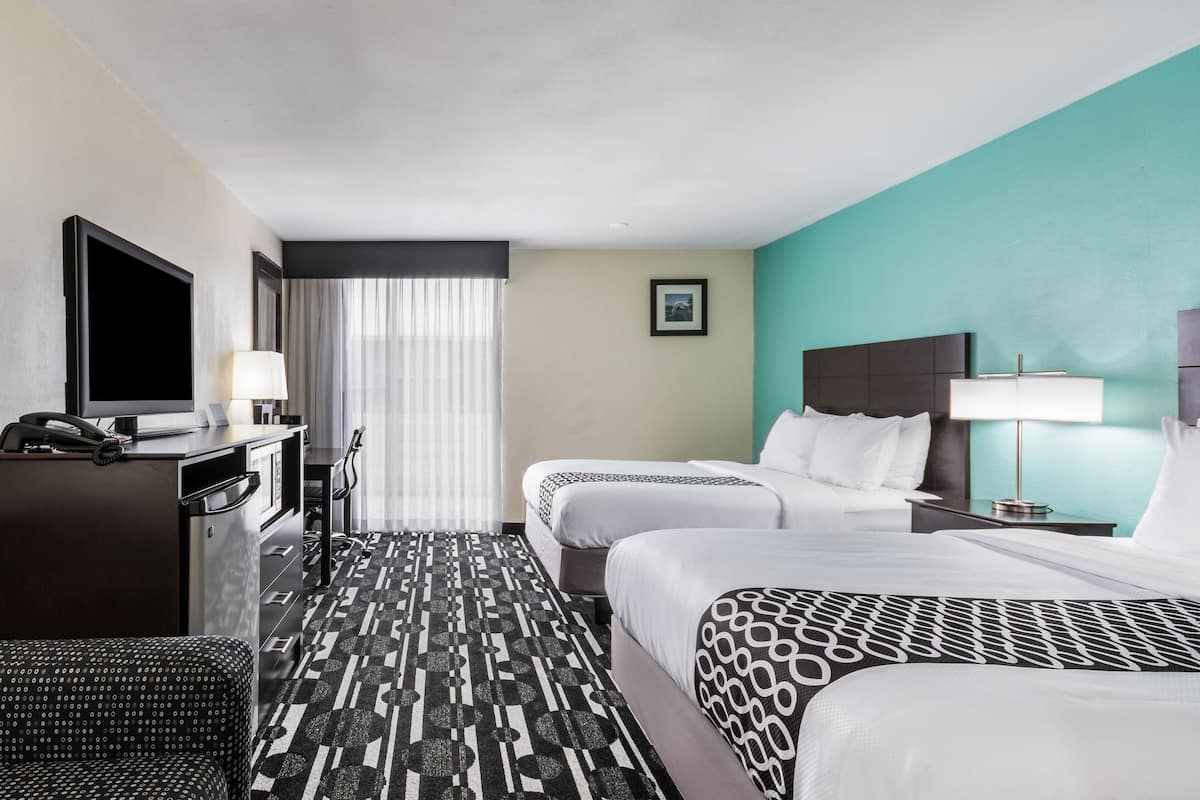 A hotel room with two beds, a desk with a telephone, a television, and a window with curtains.
