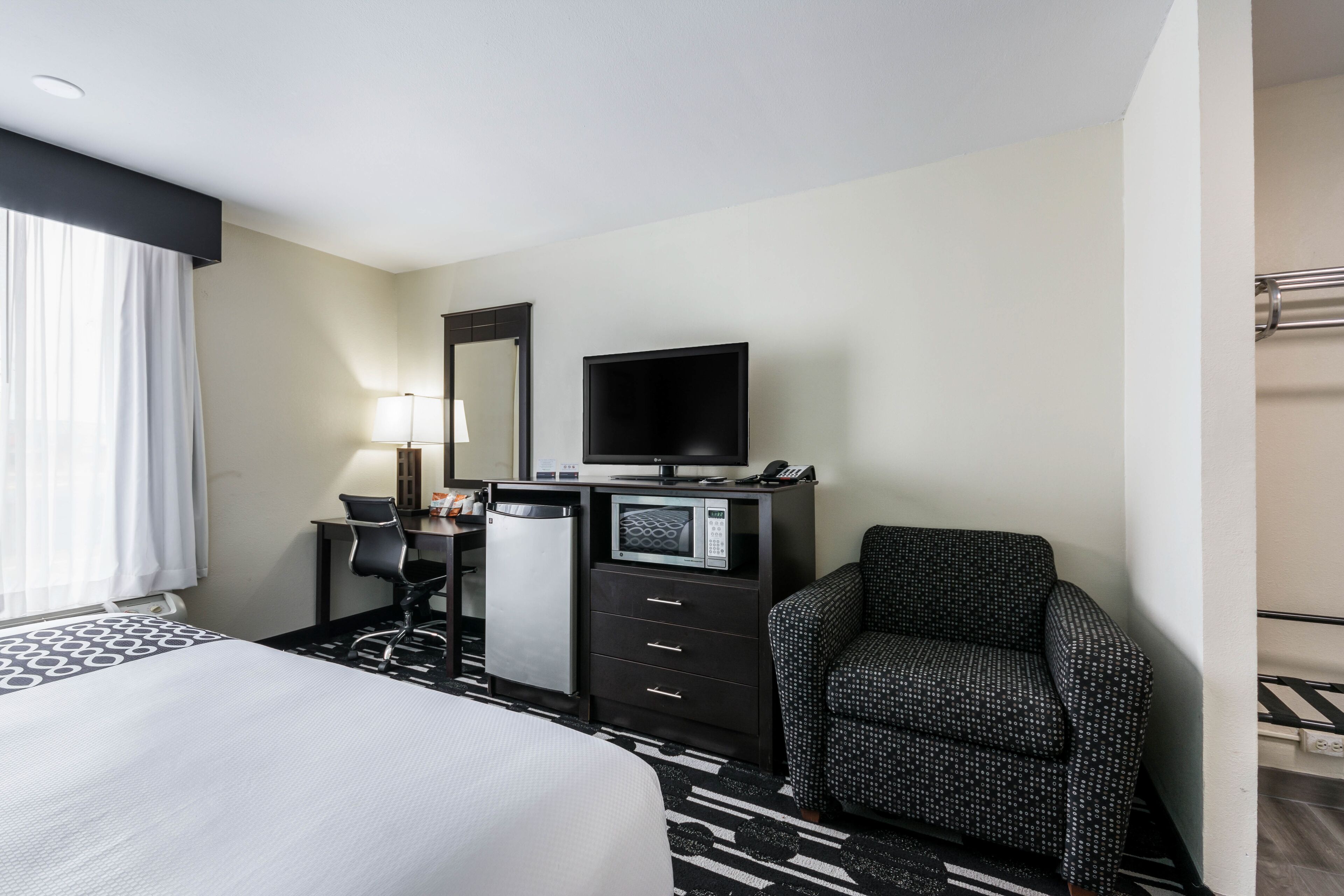 A hotel room with a bed, a desk with a computer, a microwave, a chair, and a television.