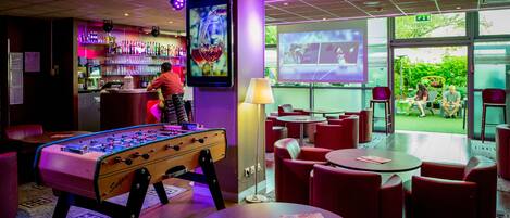 Zona de bar con mesa de fútbol, mostrador y área de estar con mesas y sillas.