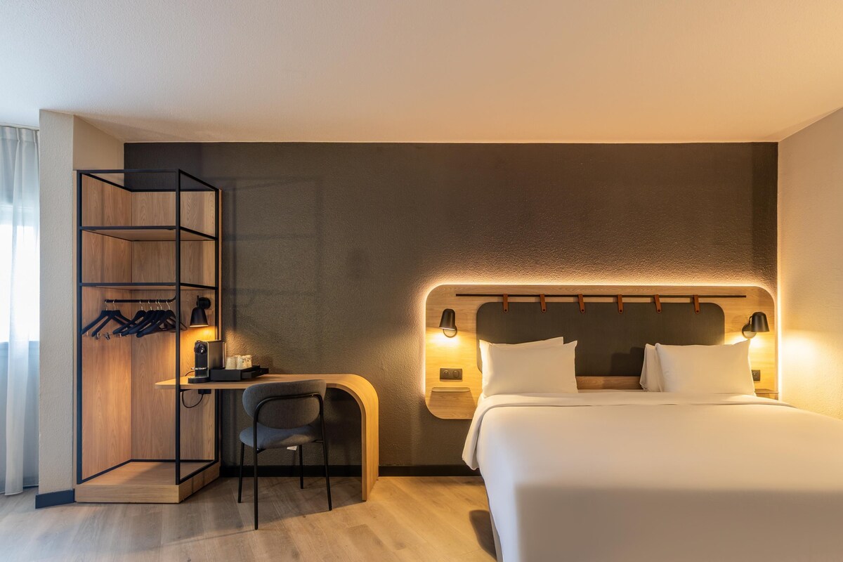 Een hotelkamer met een bed, een bureau met stoel, een kledingkast en wandlampen.