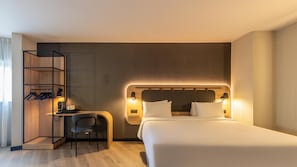 Une chambre d’hôtel comprenant un lit, un bureau avec une chaise, une armoire et des lampes fixées au mur.