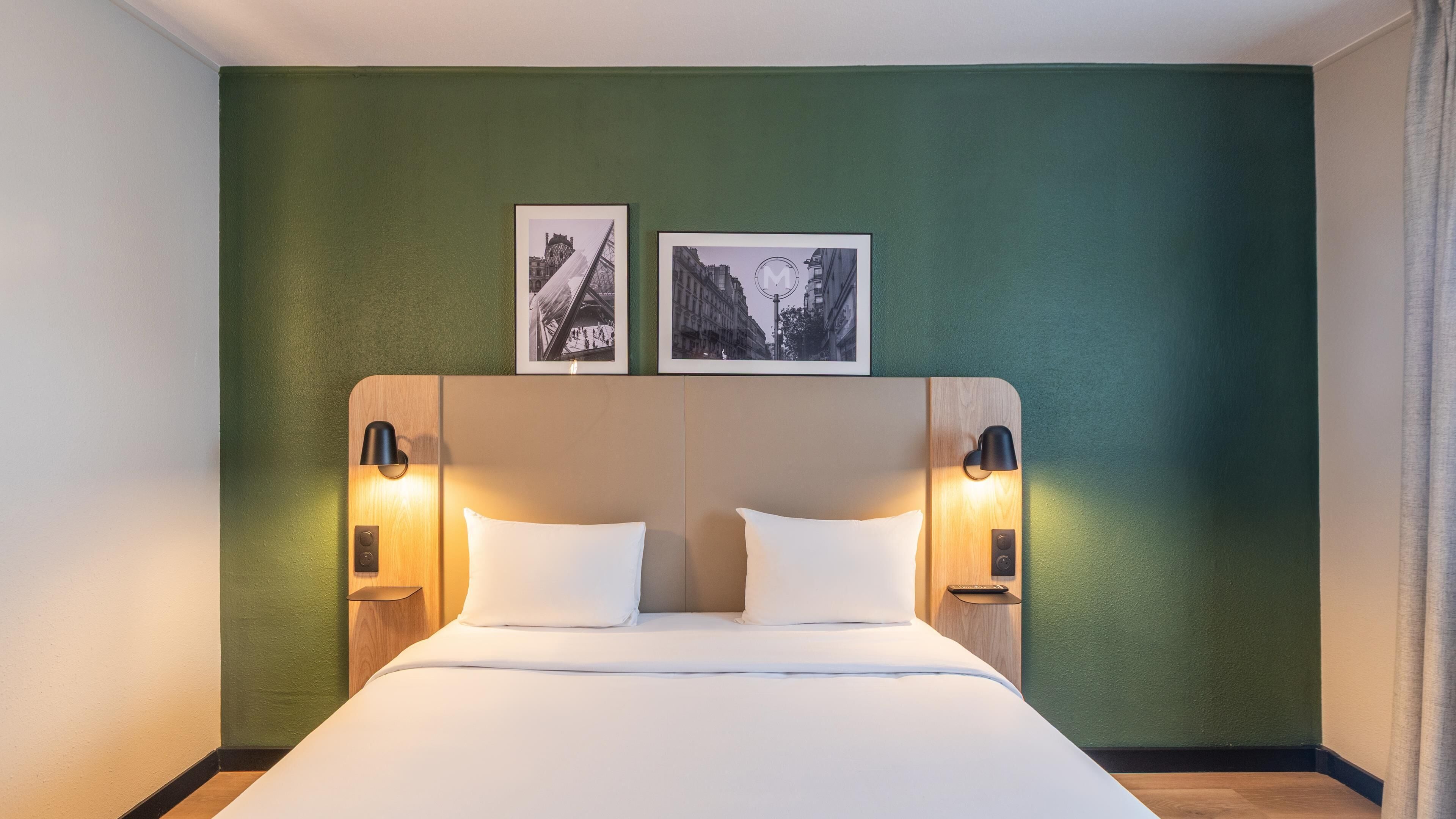 A hotel room with a large bed, two bedside tables with lamps, and two framed pictures on the wall.