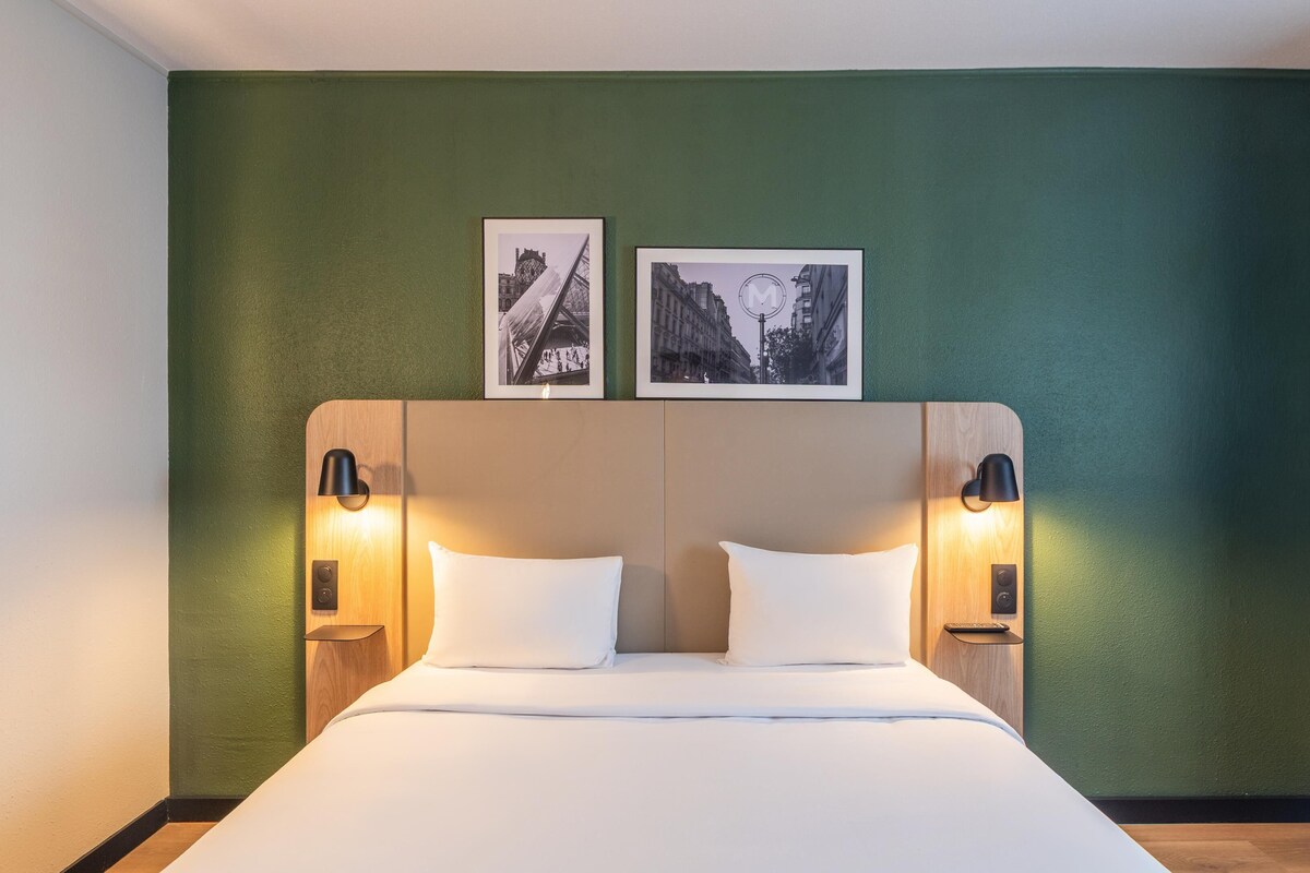 Een hotelkamer met een groot bed, twee nachtkastjes met lampen en twee ingelijste foto's aan de muur.