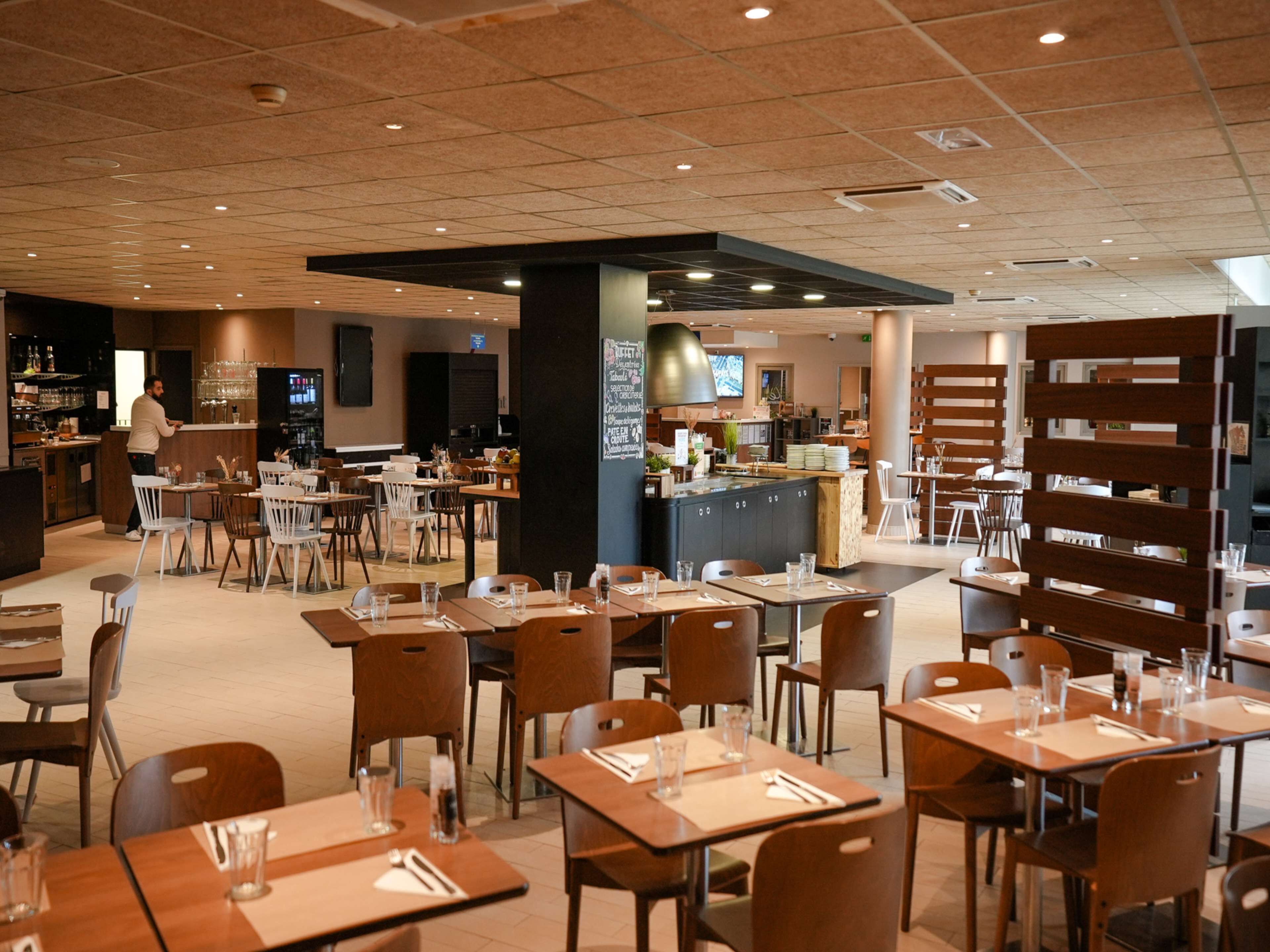 A modern restaurant with multiple dining areas, a bar, and a kitchen visible in the background.