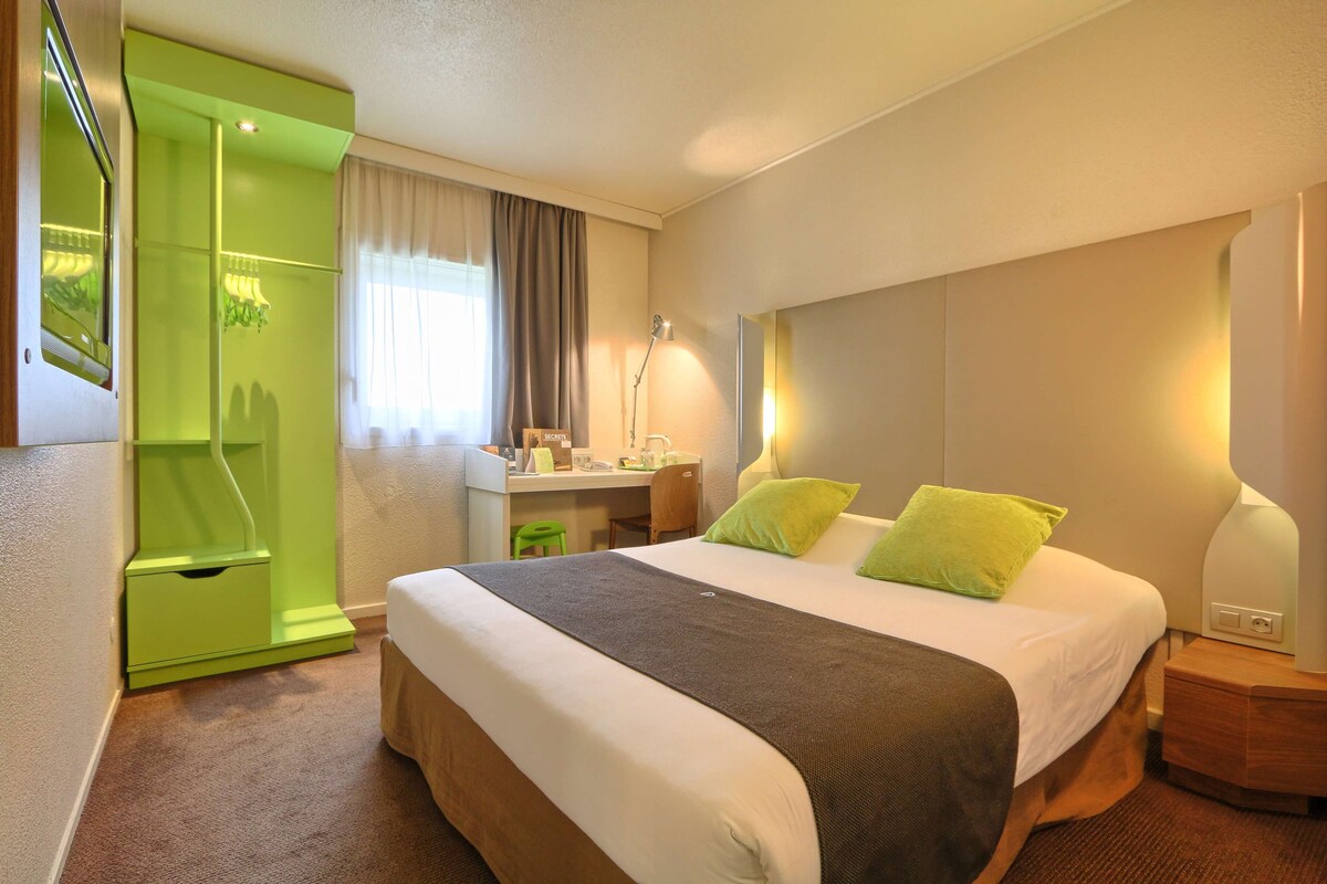 A hotel room with a bed, a desk, a green wardrobe, and a shower area.